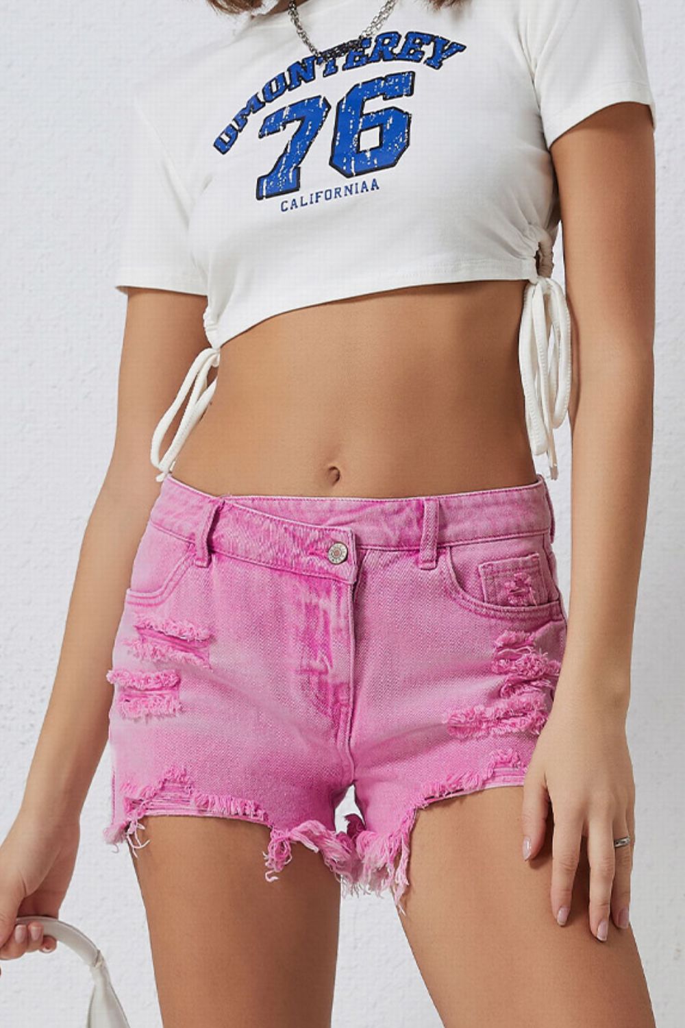 High rise crossover waist denim shorts with buttons, distressed details, and raw hem.