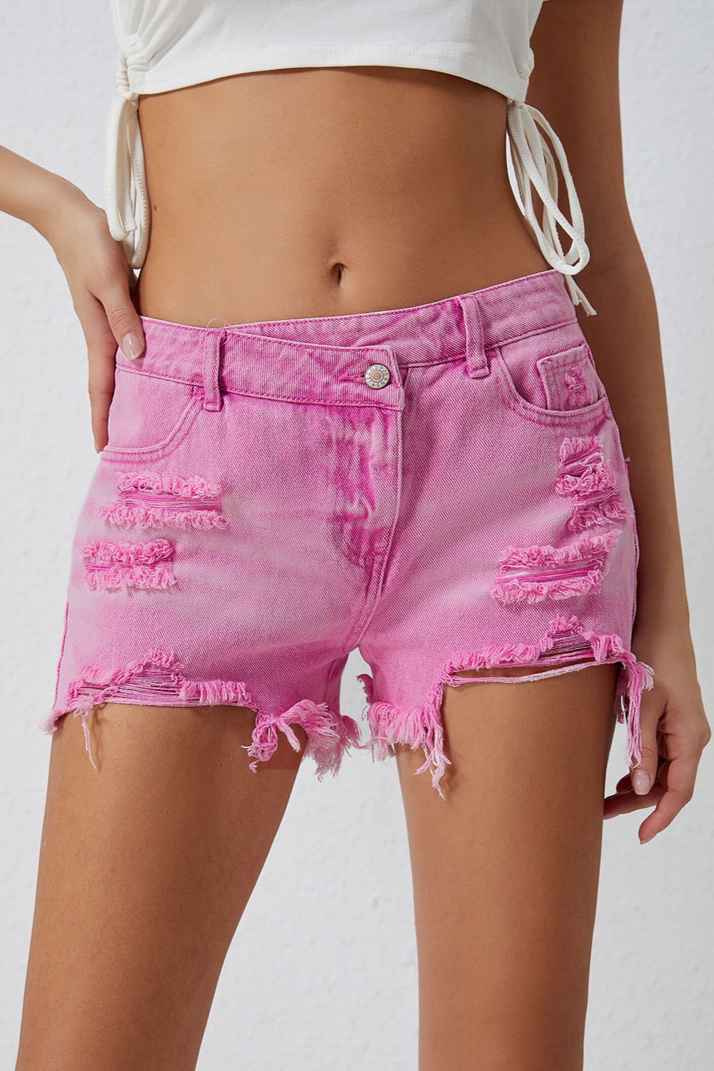 High rise crossover waist denim shorts with buttons, distressed details, and raw hem.