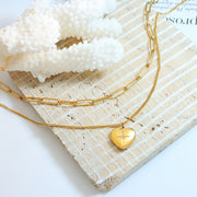 Gold-tone double-layered heart pendant necklace featuring a polished heart charm with an inlaid zircon accent and delicate chain alongside a chunky link chain.