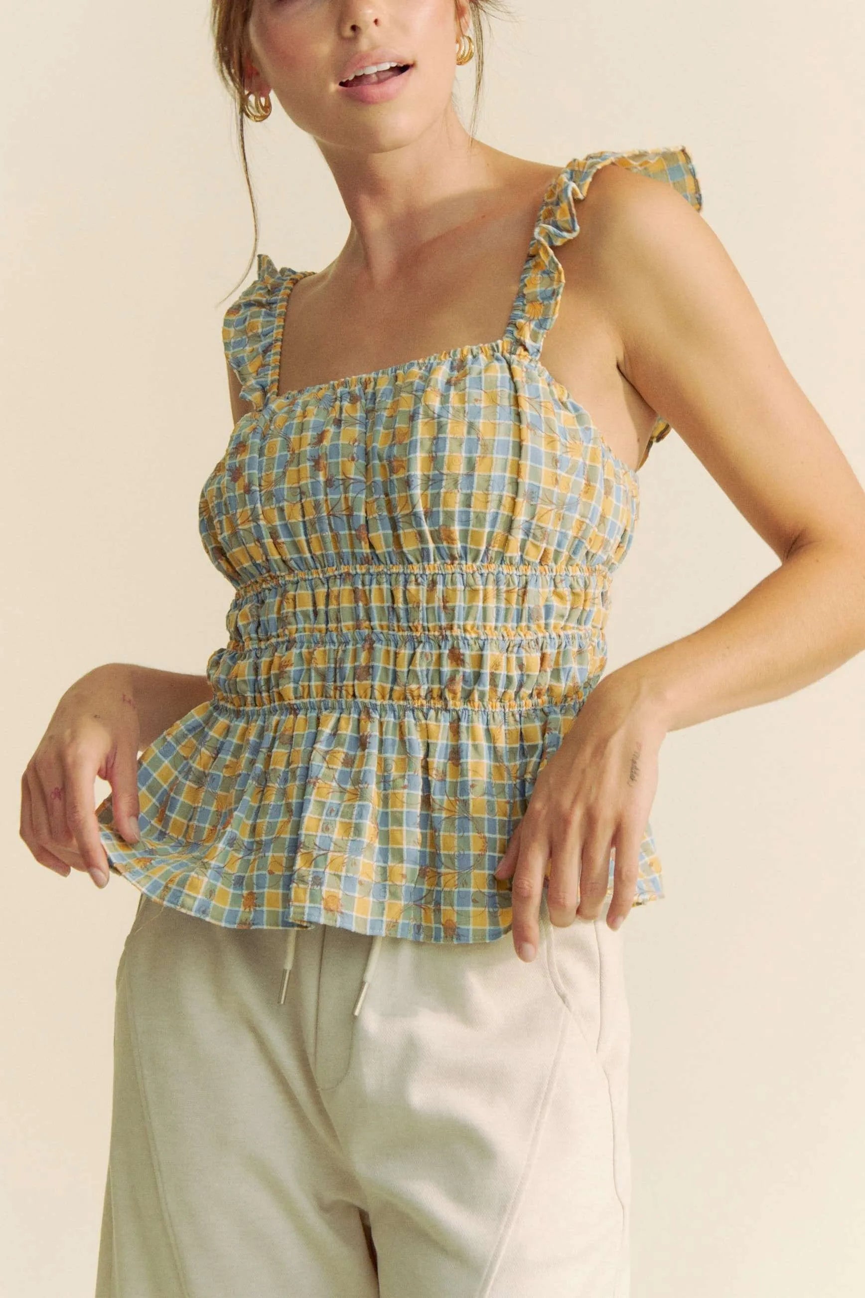 Plaid ruffled strap smocked sleeveless top with peplum, ruched details, and moderate stretch.