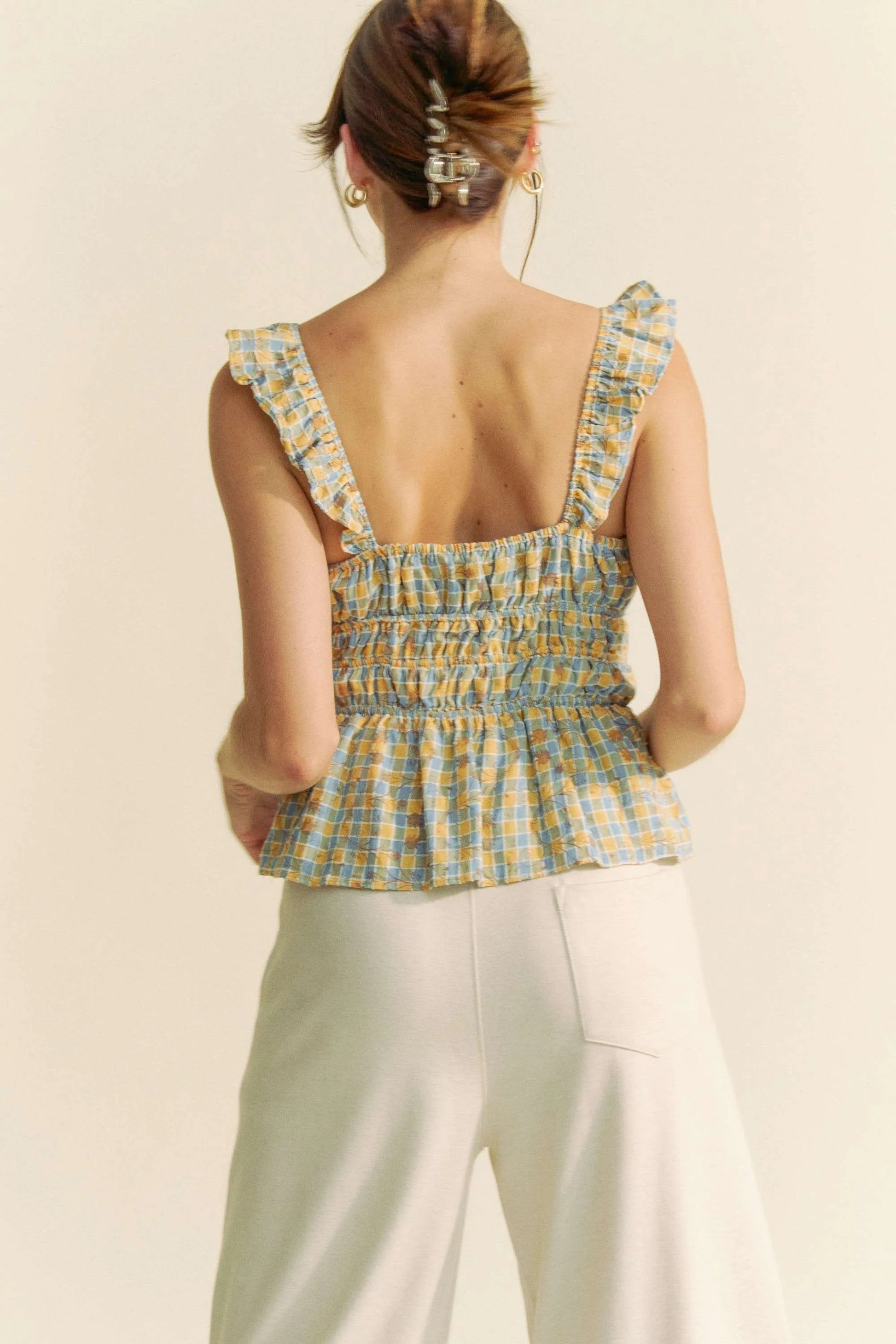 Plaid ruffled strap smocked sleeveless top with peplum, ruched details, and moderate stretch.
