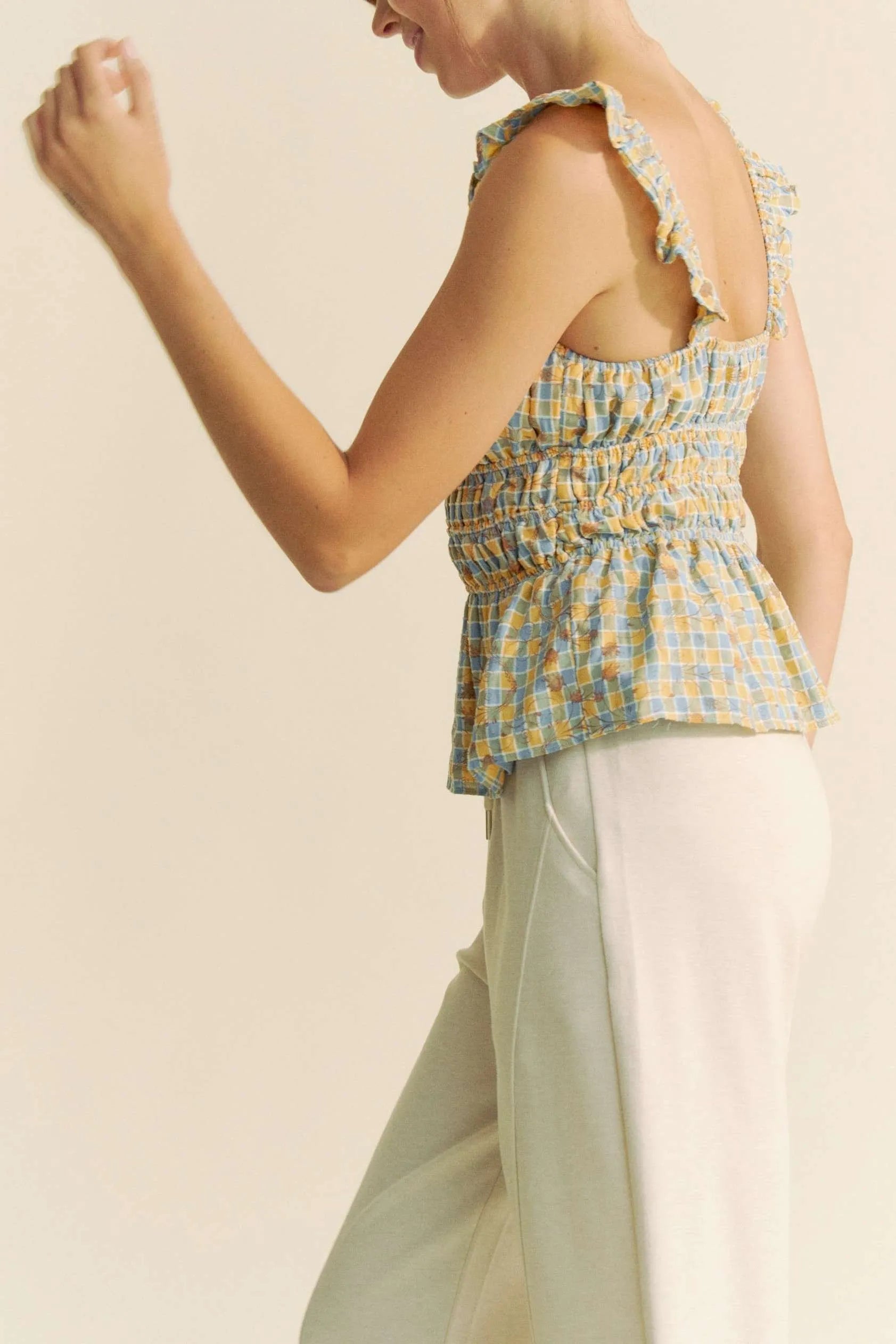 Plaid ruffled strap smocked sleeveless top with peplum, ruched details, and moderate stretch.