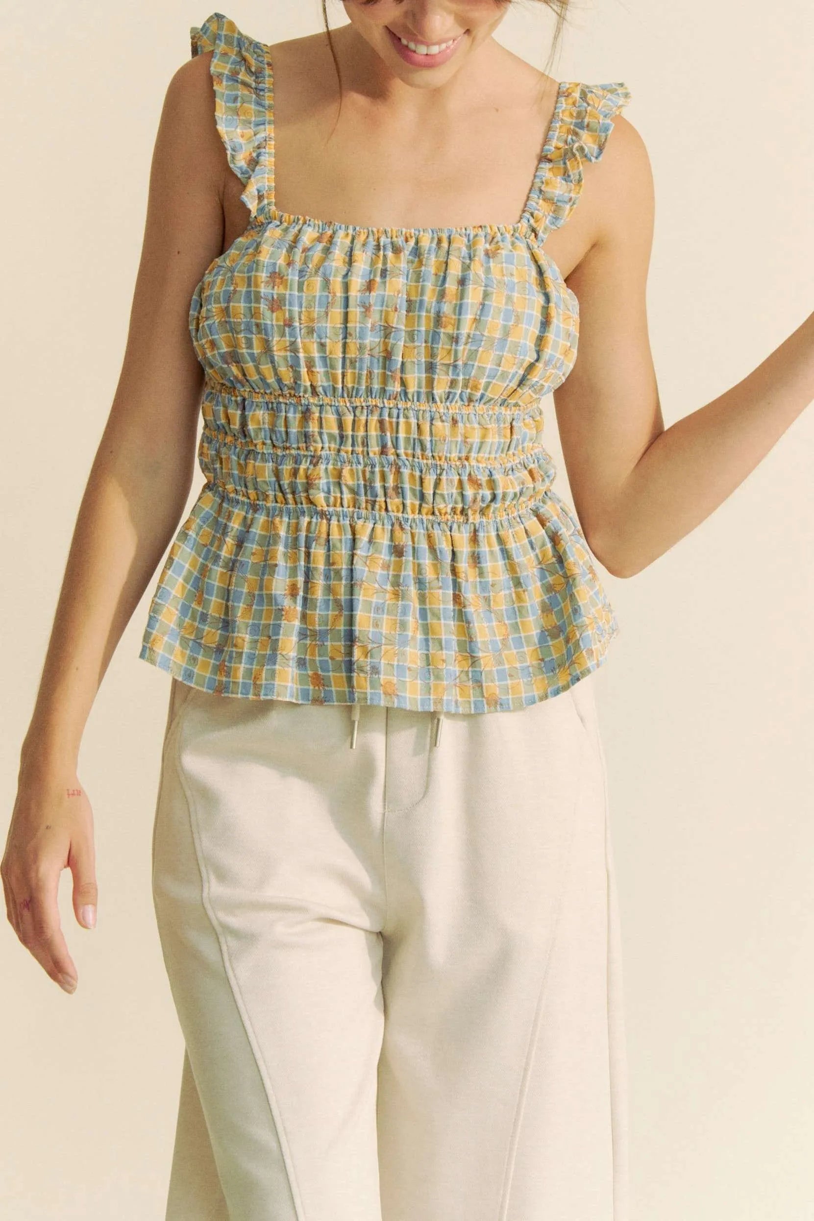 Plaid ruffled strap smocked sleeveless top with peplum, ruched details, and moderate stretch.