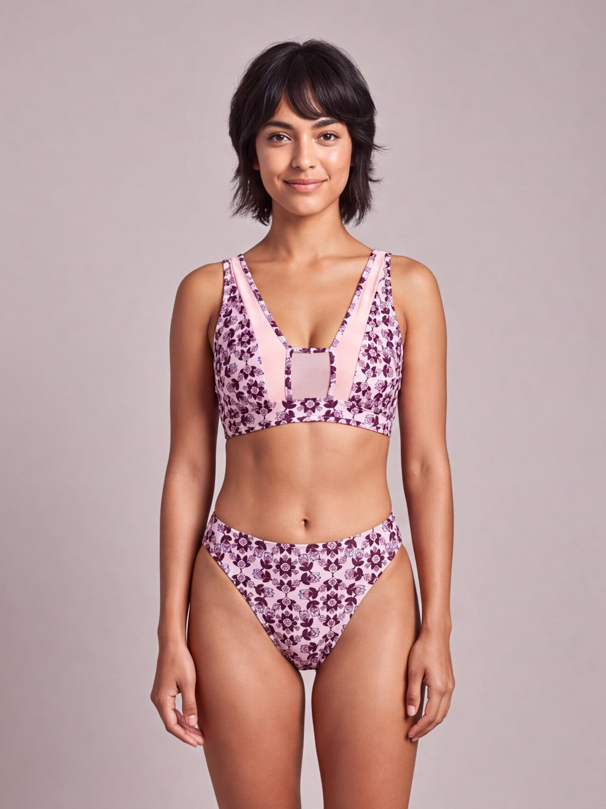 Model stands facing forward in a printed pink and purple two-piece bikini with wide straps, a structured crop top, and high-cut bottoms.