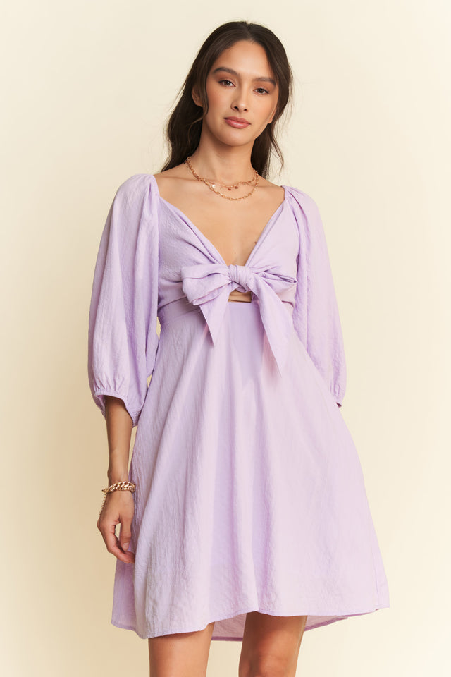 Woman wearing a light purple dress with a bow detail on a beige background