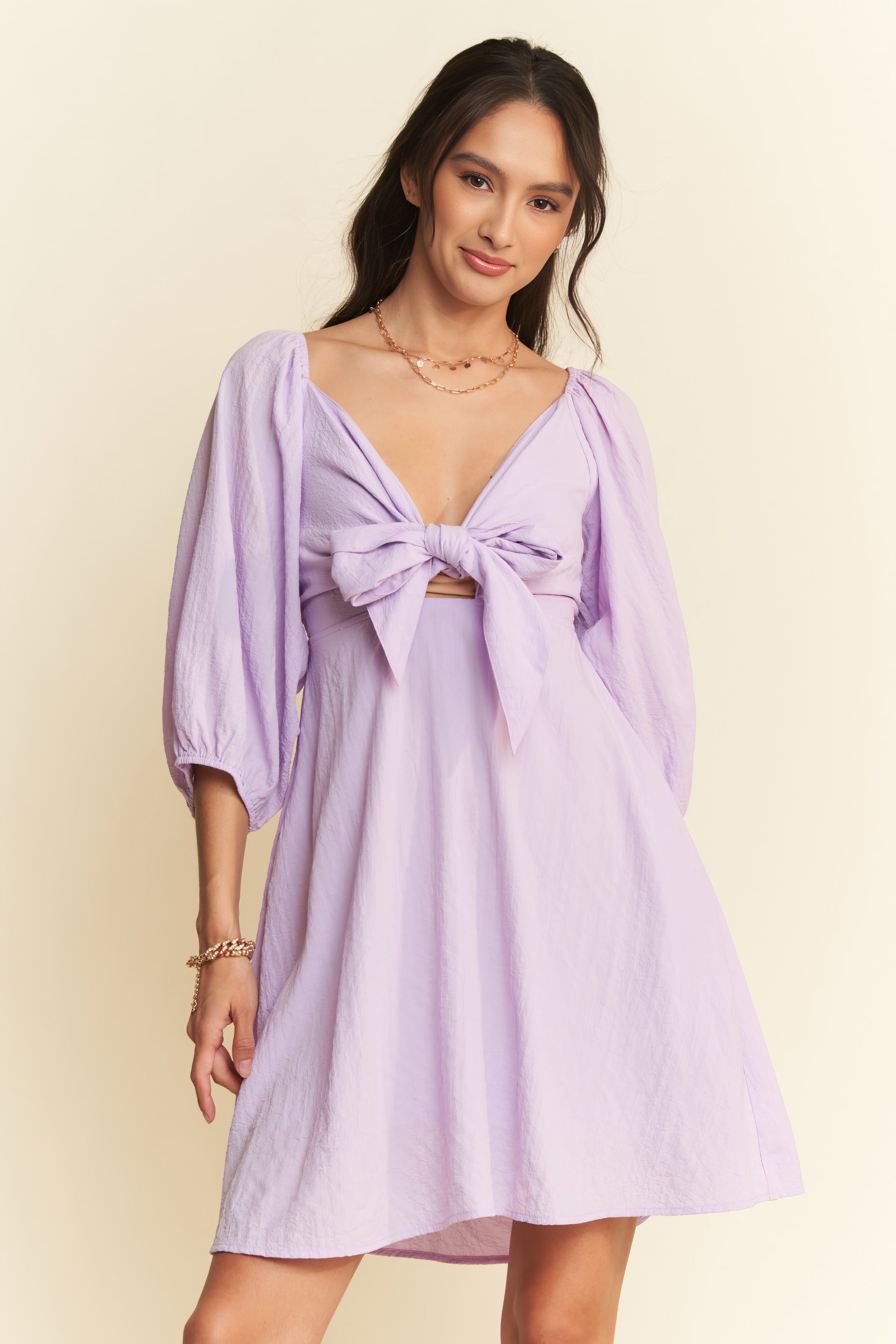Woman wearing a light purple dress with a bow detail on a beige background