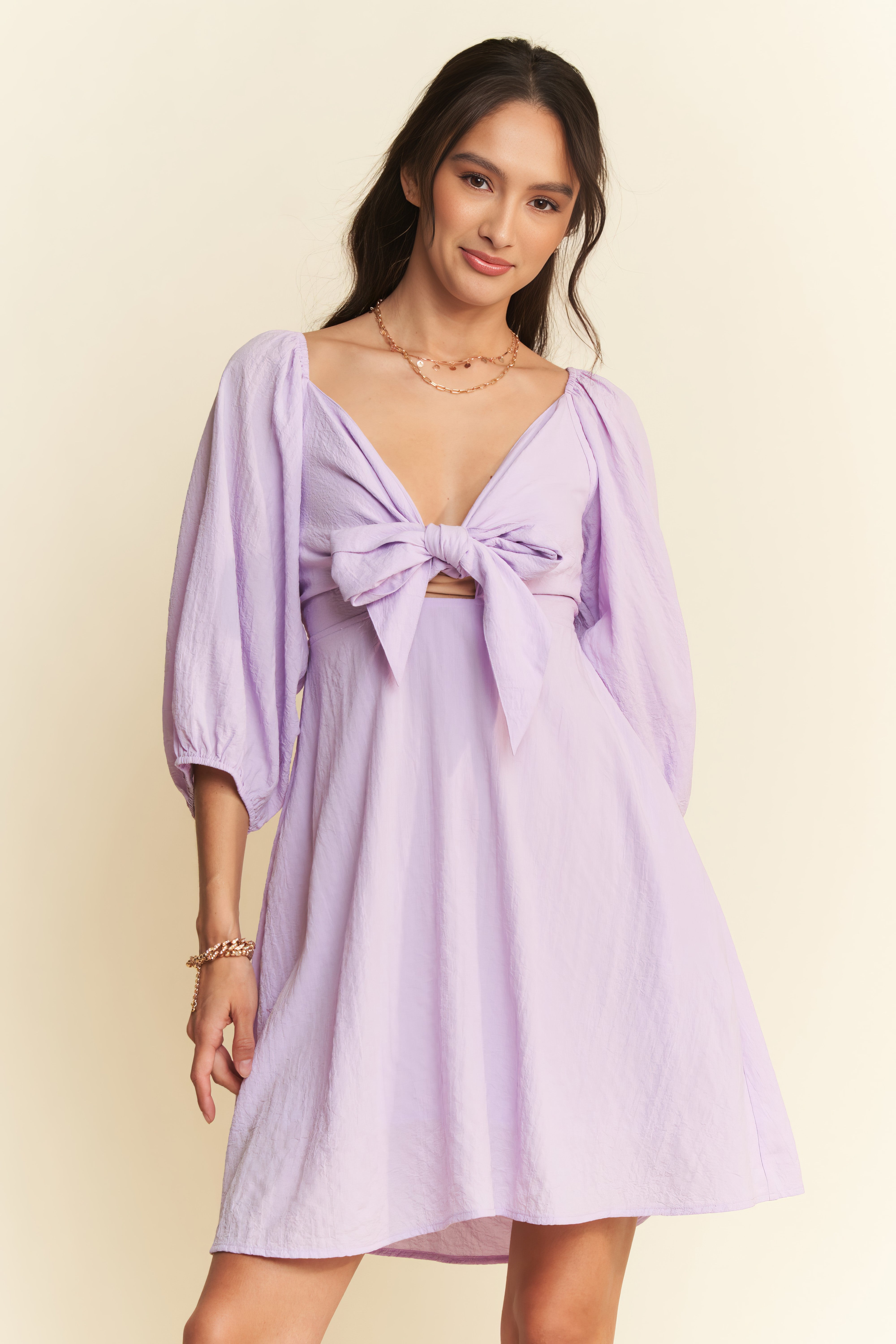 Woman wearing a light purple dress with a bow detail on a beige background