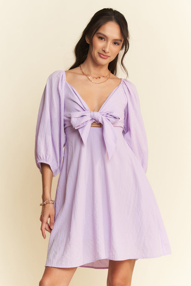 Woman wearing a light purple dress with a bow detail on a beige background