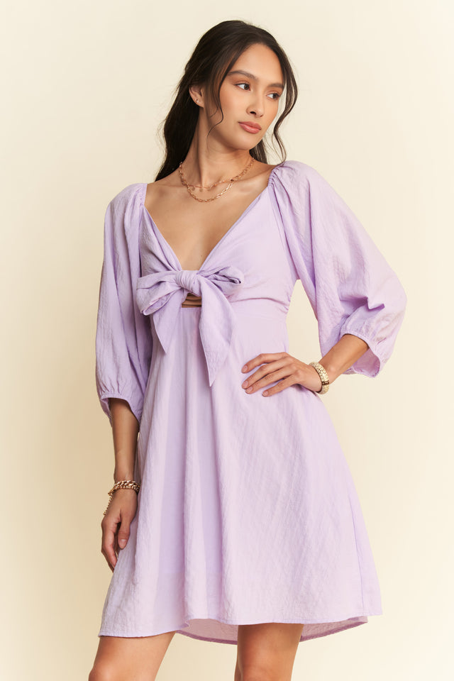 Woman wearing a light purple dress with a belt on a beige background