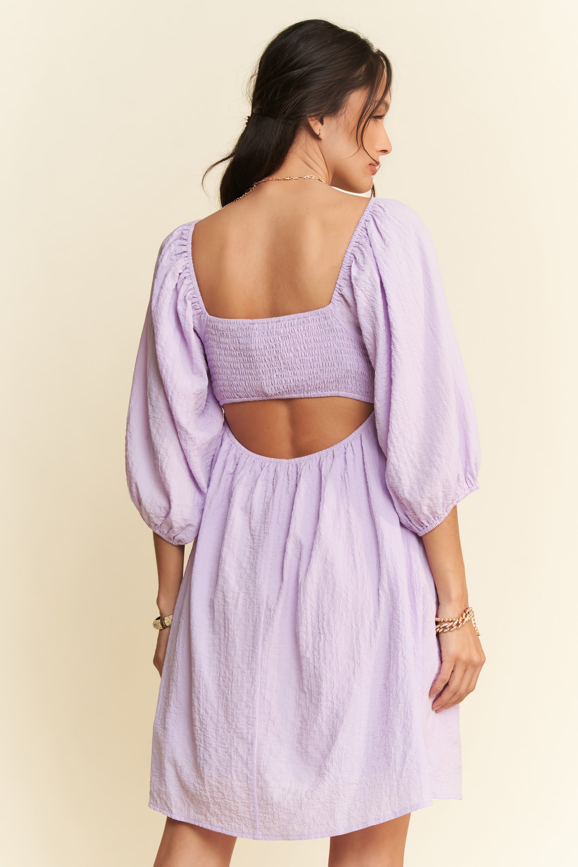 Woman wearing a light purple dress with a backless top on a beige background