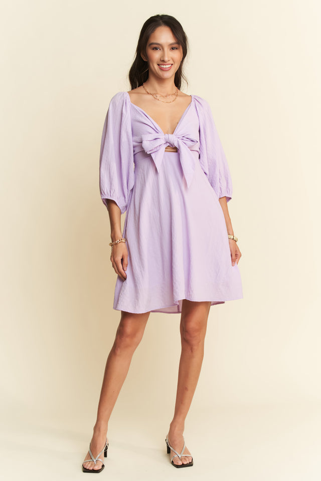 Woman wearing a light purple dress with a bow detail on a beige background