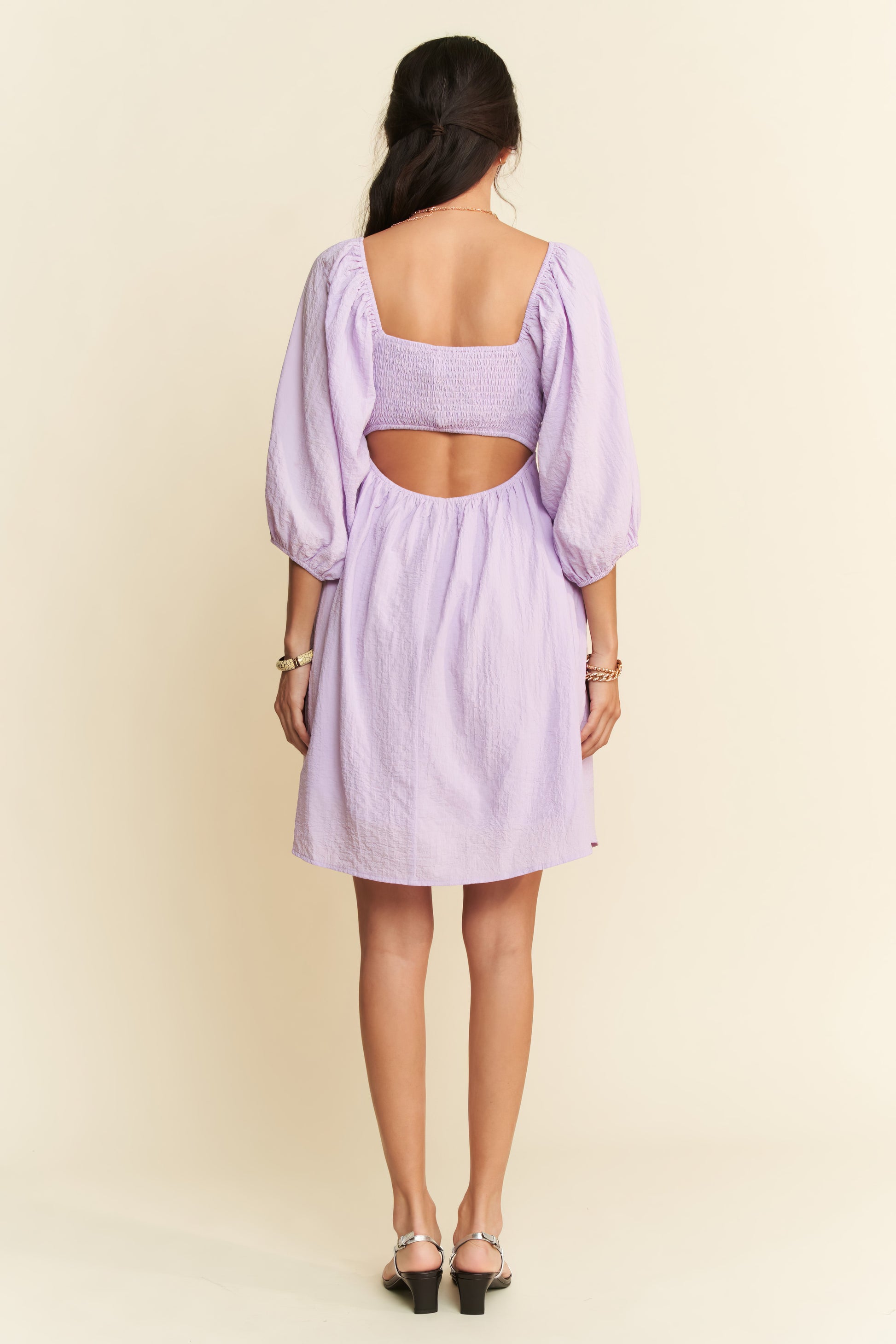 Woman wearing a light purple dress with cut-out back on a beige background