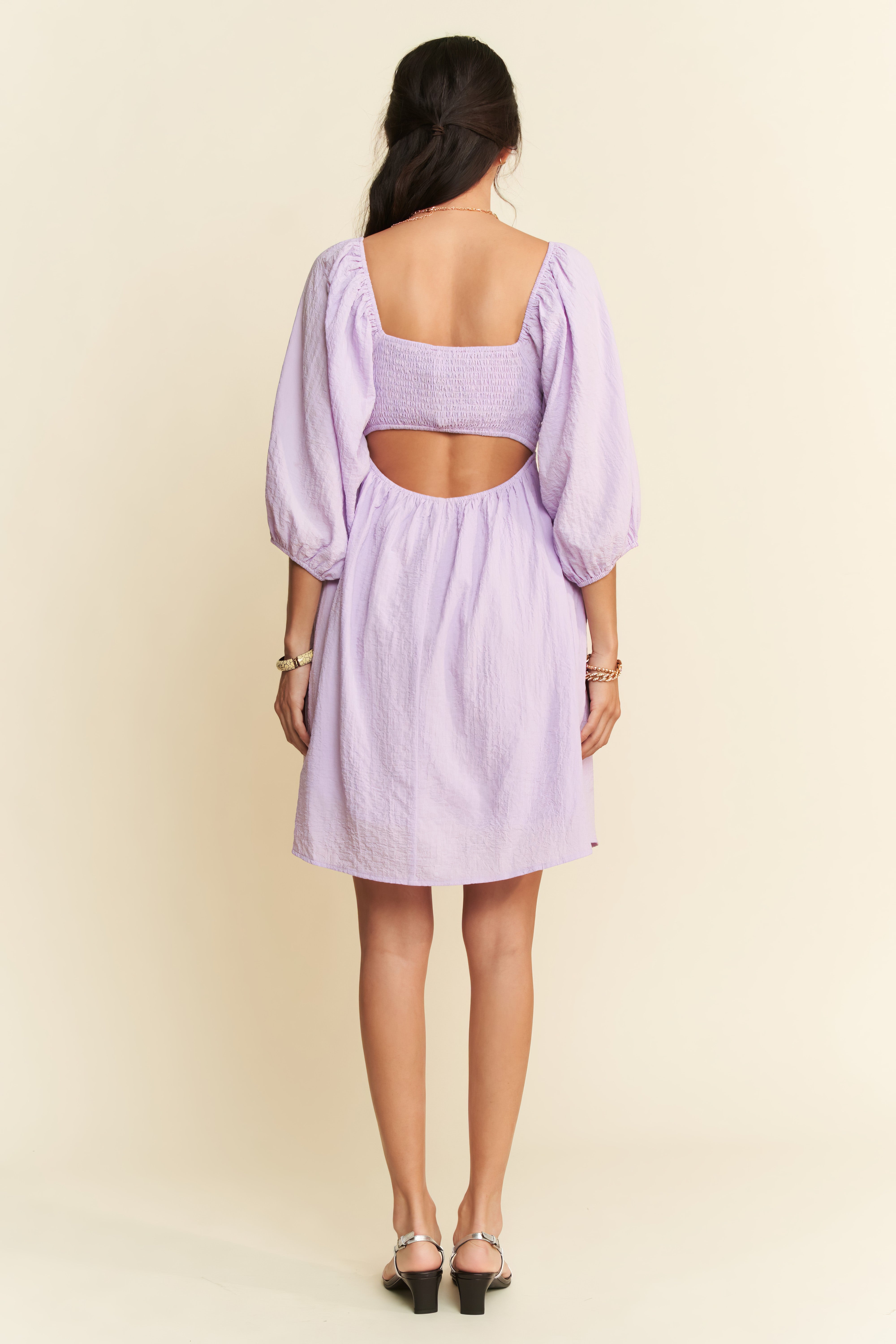 Woman wearing a light purple dress with cut-out back on a beige background