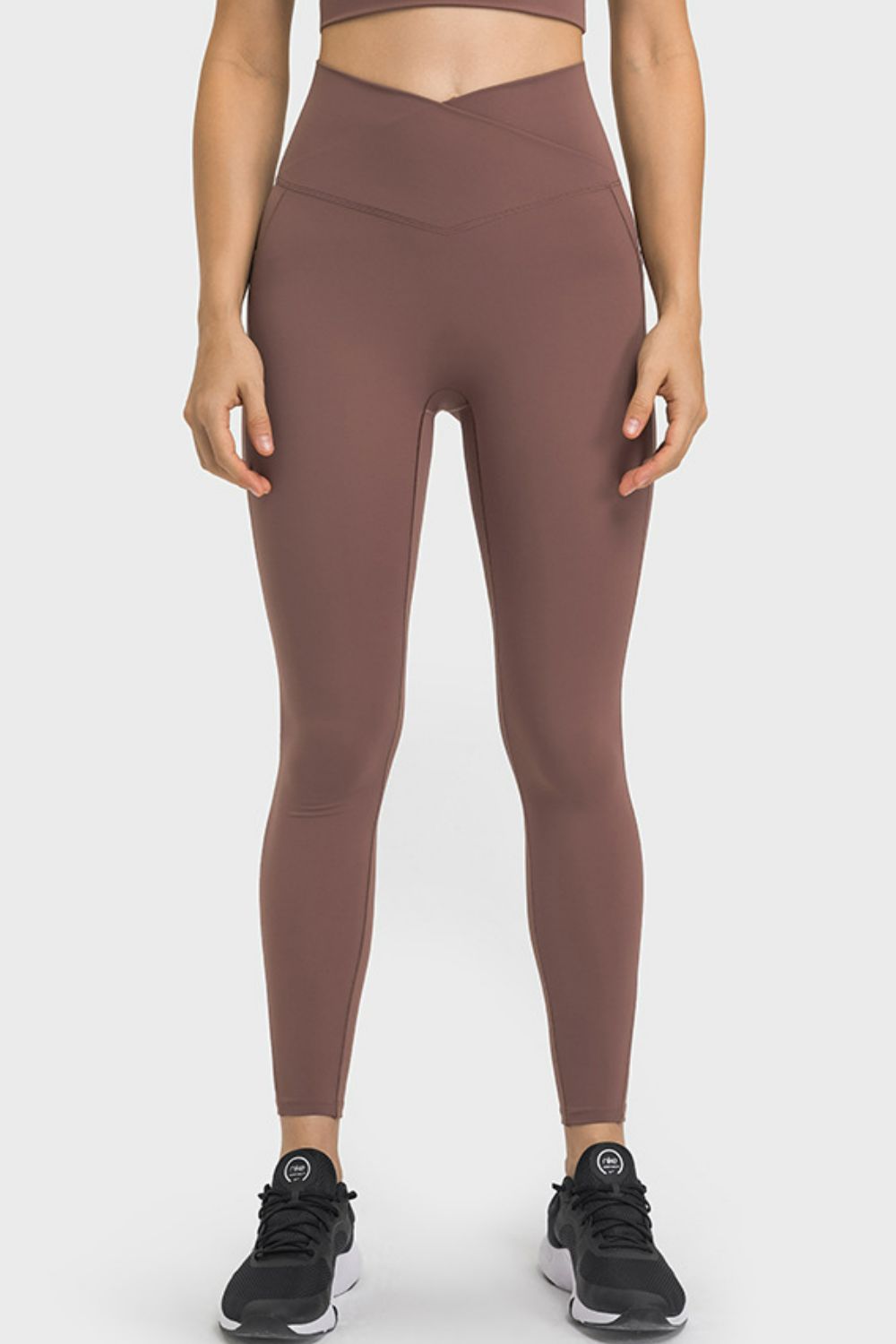 Model stands with hands at her sides wearing brown V-waist yoga leggings with a fitted full-length silhouette and visible contoured seams.