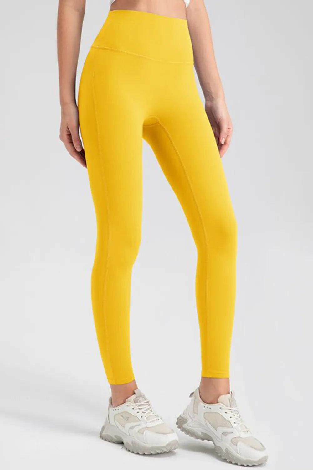 Model standing in bright yellow high-waist skinny active pants with a close-fitting full-length silhouette, smooth seamed construction, and one foot angled forward.
