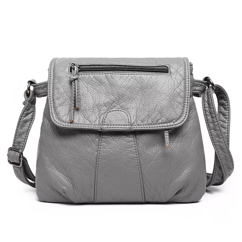 Small gray PU leather crossbody bag with an adjustable strap, flap closure, top zip pocket, stitched panels, and a structured rounded silhouette.