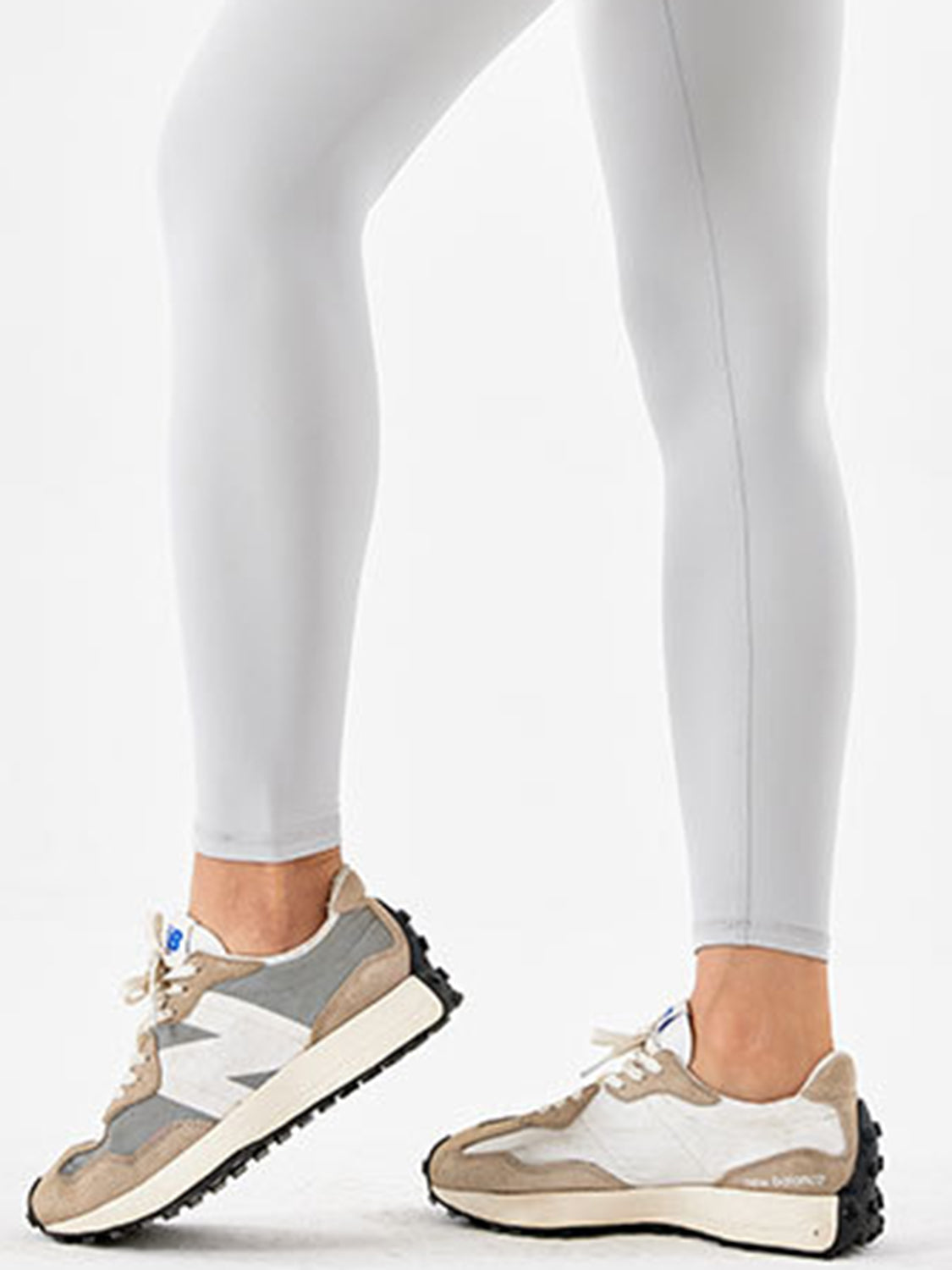 A model wears white, full-length sports leggings with a close, stretchy silhouette, standing with one foot angled forward to show the ankle-length fit.