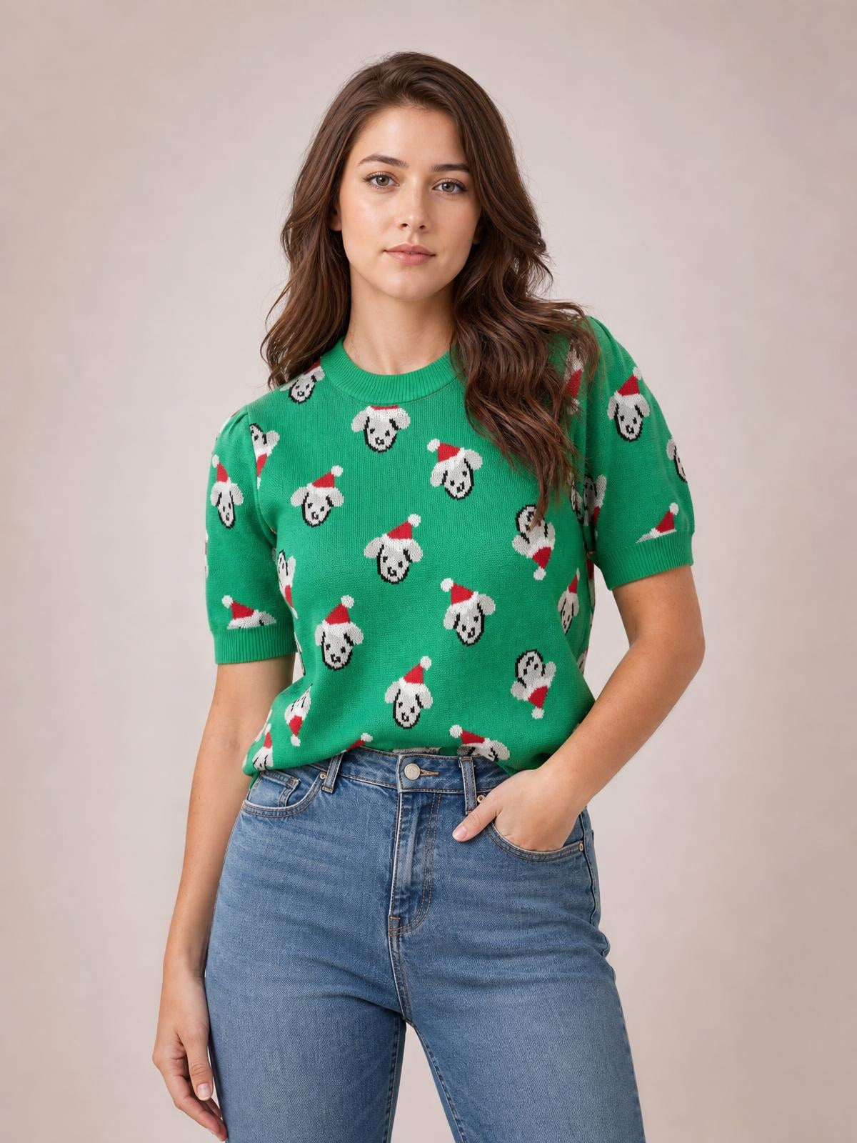 Model wears a green Christmas sweater with an abstract dog pattern, round neck, short sleeves, ribbed trim, and a relaxed silhouette, posing with one hand in her jeans pocket.