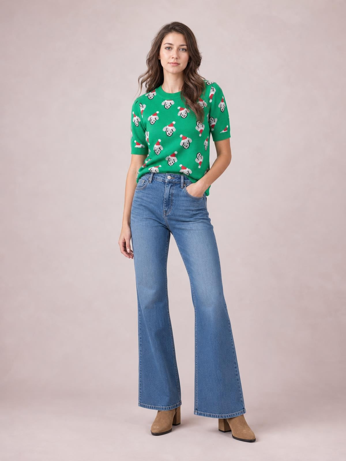 Model poses with one hand in her pocket wearing a green round-neck Christmas sweater with short sleeves and an abstract dog pattern.