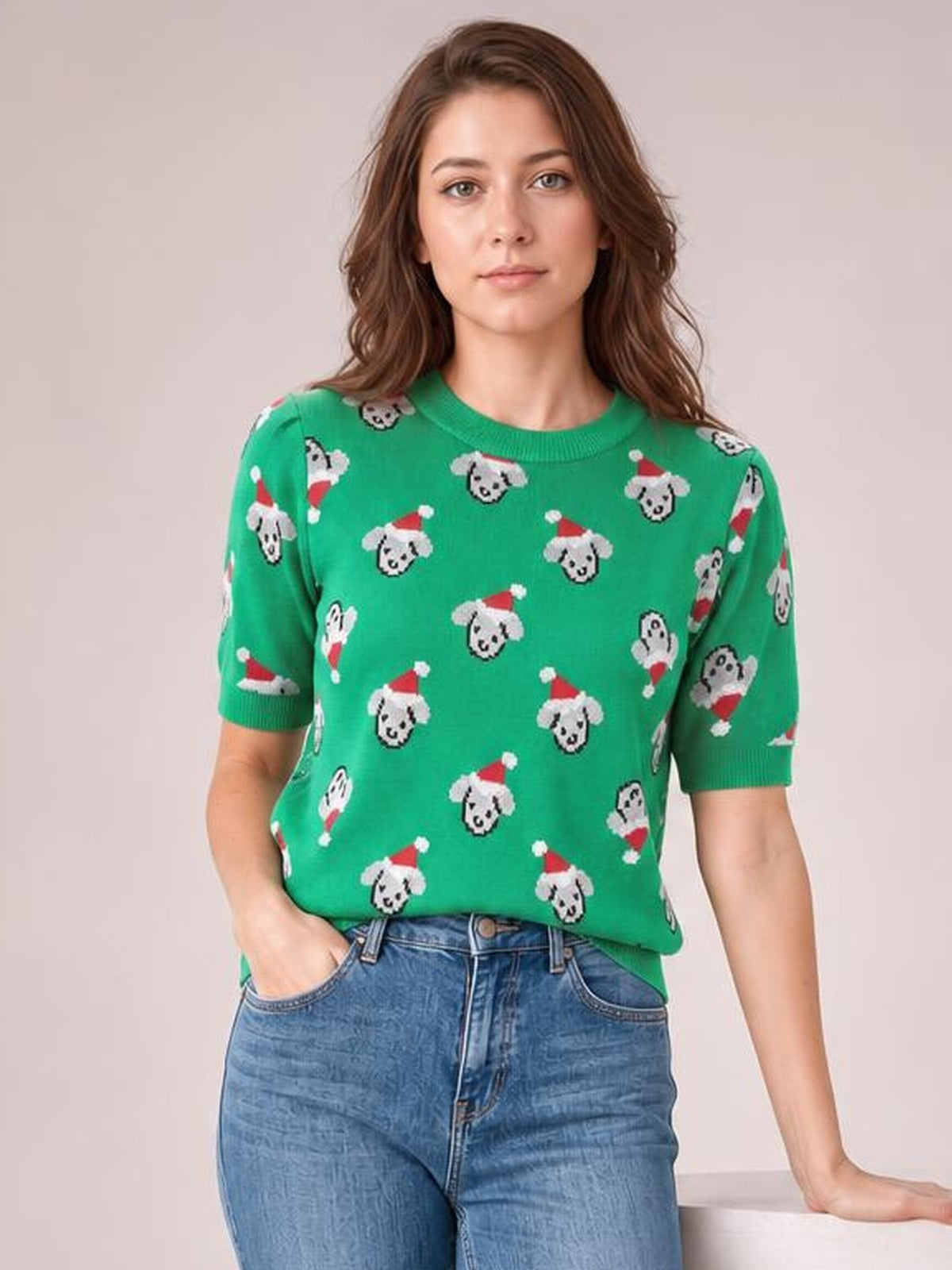 A woman models a green Christmas sweater with a round neck, short sleeves, and an allover pattern of dogs wearing Santa hats.