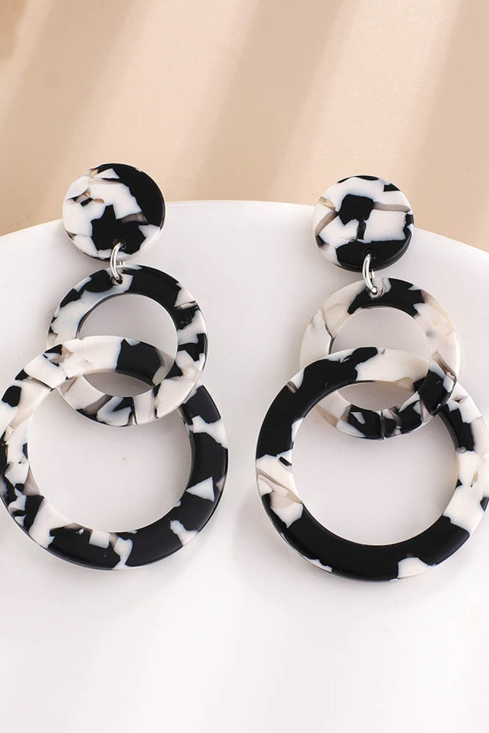 Black-and-white marbled acrylic double-hoop earrings feature layered circular hoops and a bold sculptural silhouette for statement styling.