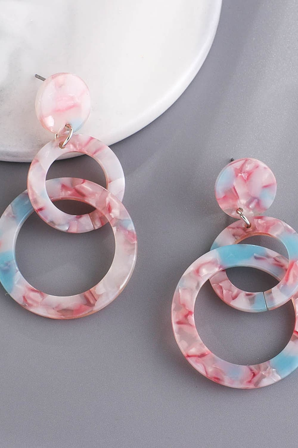 Acrylic double-hoop earrings feature round tops and layered circular hoops in a translucent pink-and-blue marbled finish.