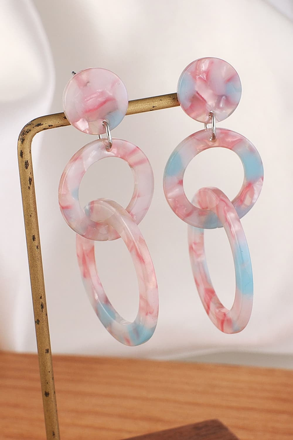 Pink and blue marbled acrylic double-hoop earrings feature round stud tops, linked circular hoops, and elongated dangling loops for a sculptural statement silhouette.