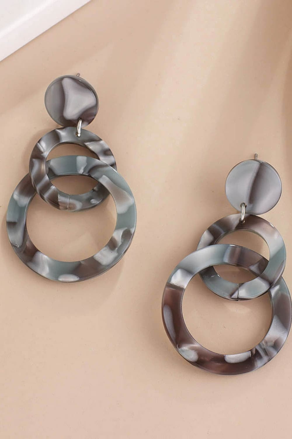 A pair of smoky gray acrylic double-hoop earrings features layered circular hoops and rounded stud tops in a sculptural, statement-making silhouette.