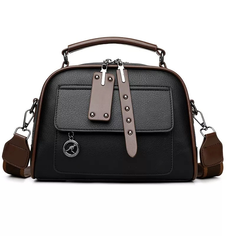 Small black PU leather crossbody bag with brown trim, an adjustable shoulder strap, top handle, zip closure, front pocket, and decorative strap details.