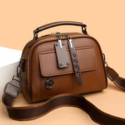 Small brown PU leather crossbody bag with an adjustable woven strap, top handle, structured silhouette, front pocket, and dual zipper closures.