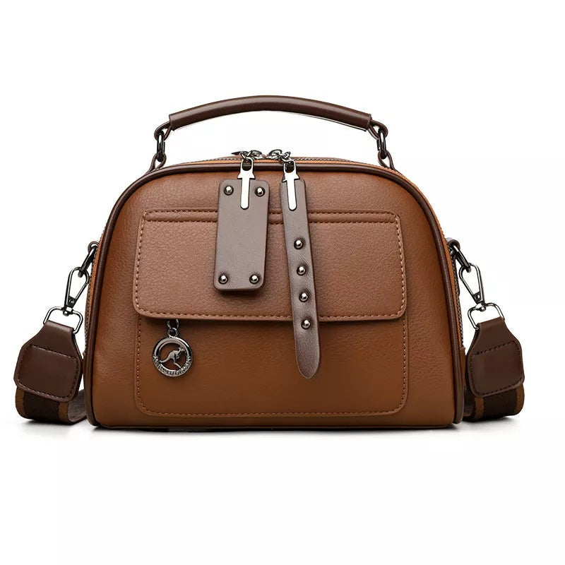 Small brown PU leather crossbody bag with an adjustable strap, top handle, dual zippers, front flap pocket, and decorative vertical strap detailing.