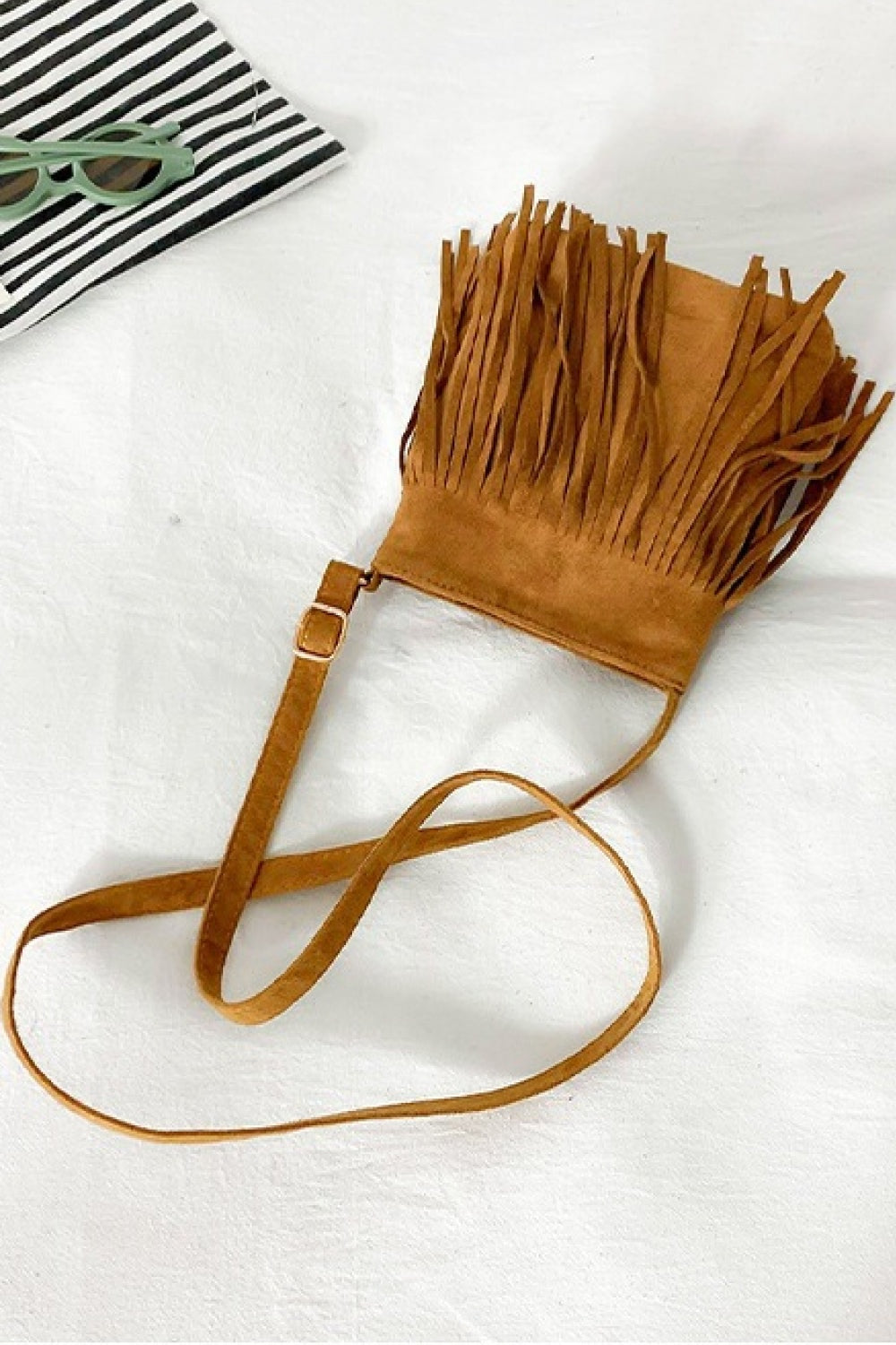 Small tan PU leather crossbody sling bag with a compact silhouette, adjustable strap, buckle detail, and dramatic long fringe across the front.