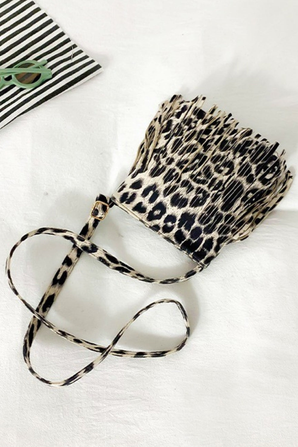 A small leopard-print PU leather crossbody bag features a compact rectangular silhouette, long fringe detailing, and a slim adjustable strap.