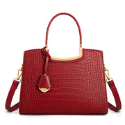 Medium red crocodile-embossed PU leather top-handle handbag with a structured silhouette, gold-tone hardware, decorative tag, and shoulder strap.