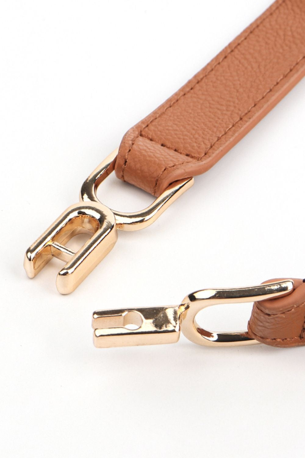 Close-up of a slim tan PU elastic belt with textured finish, stitched edges, and a polished interlocking alloy buckle.