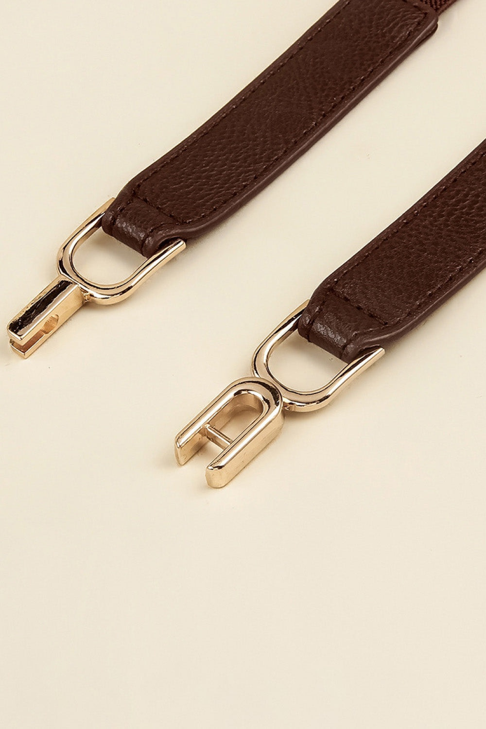 Slim brown textured PU elastic belt with stitched edges and a polished alloy interlocking buckle, showcasing its refined construction and sleek silhouette.