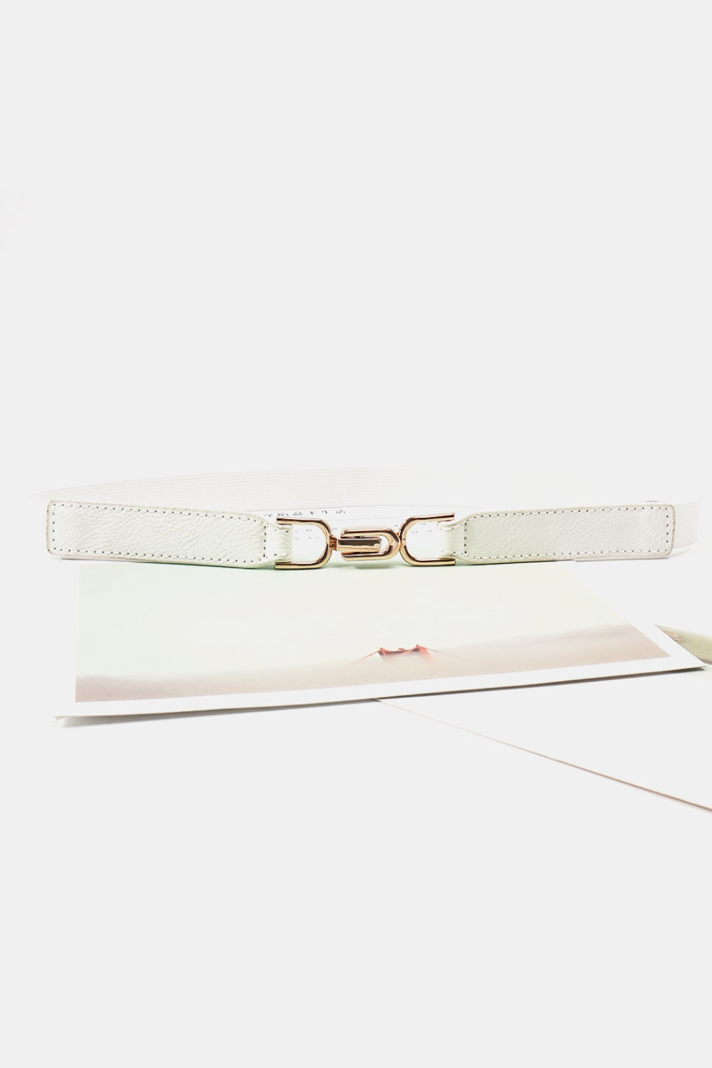 A slim white elastic belt with textured PU panels, stitched edges, and a sculptural rose-gold-tone interlocking alloy buckle.