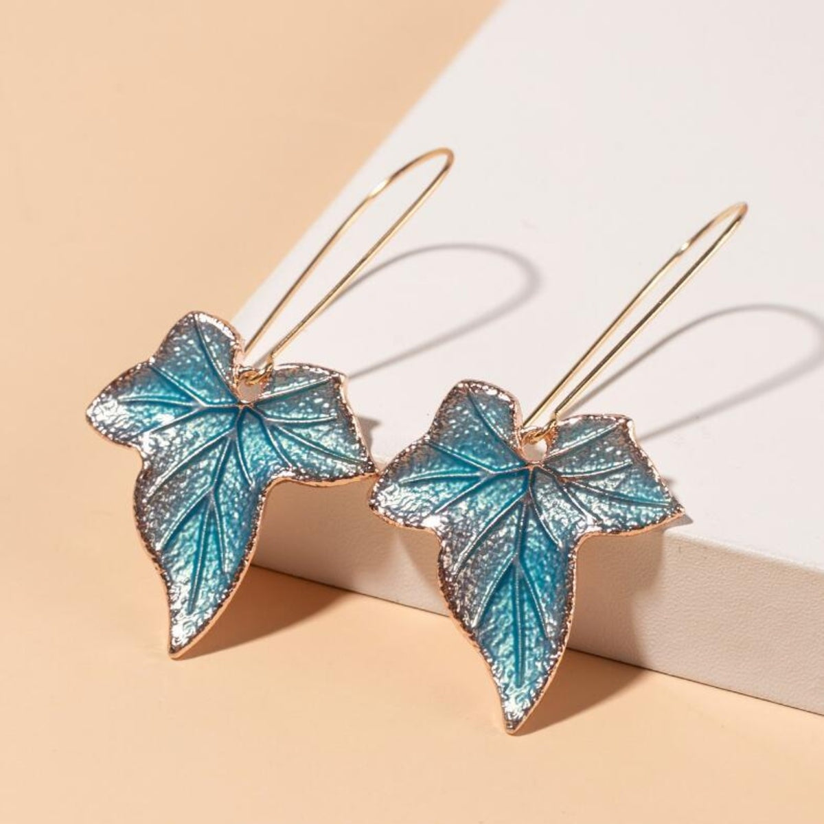 Blue and silver-toned alloy leaf drop earrings feature textured, veined silhouettes with elongated gold-tone hooks and graceful sculptural movement.
