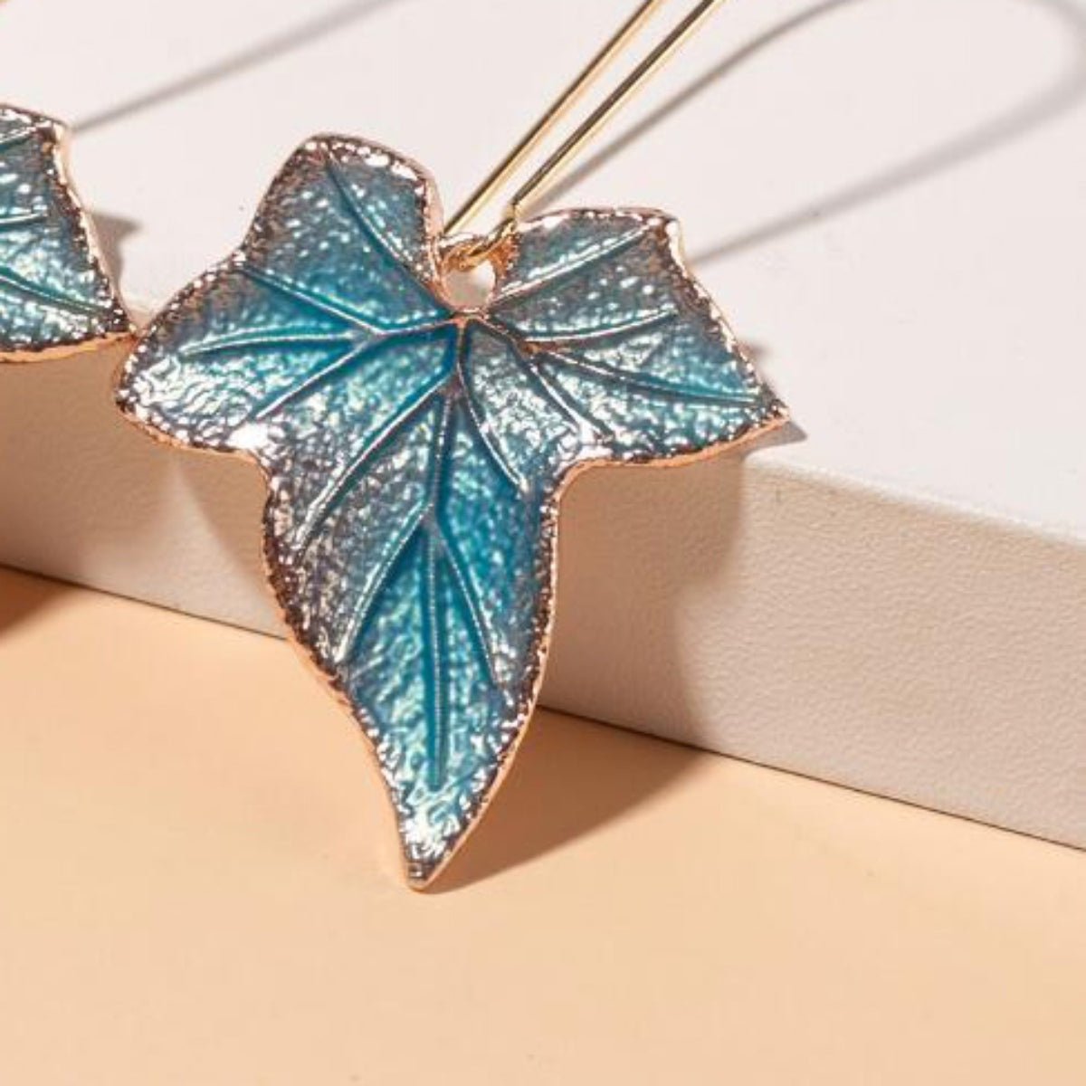 Textured teal-blue alloy leaf drop earrings feature sculpted veining, gold-tone edges, and an elongated botanical silhouette.
