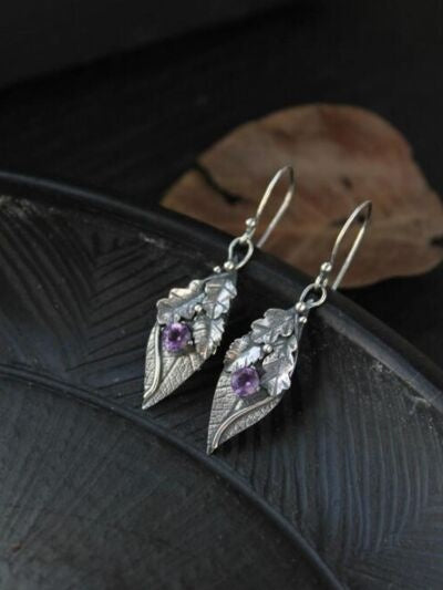Silver-toned alloy leaf-shaped drop earrings feature textured botanical construction, open ear wires, and purple rhinestone accents for a graceful statement finish.