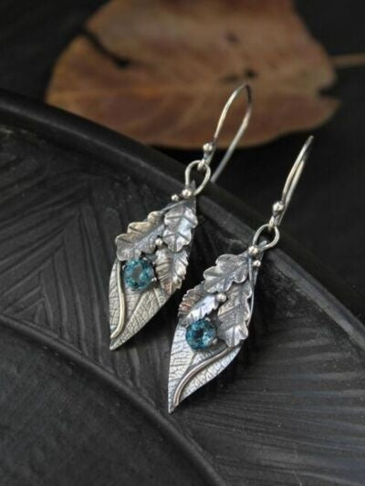 Leaf-shaped alloy dangle earrings feature layered silver-tone leaves, faceted rhinestone accents, and blue center stones for a botanical statement.