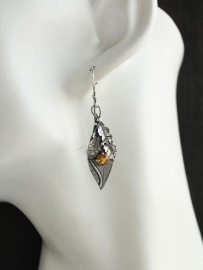 A silver-toned alloy leaf-shaped earring hangs from the ear, featuring layered botanical construction and faceted rhinestone detailing with a warm amber accent.