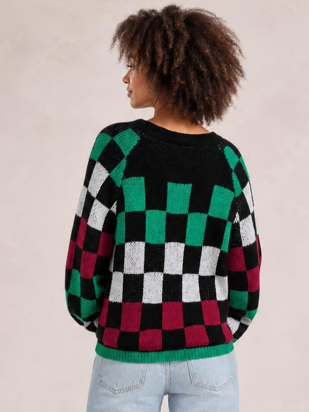 A model shown from behind wears a relaxed checkered sweater in black, green, white, and burgundy with loose lantern sleeves and a ribbed green hem.