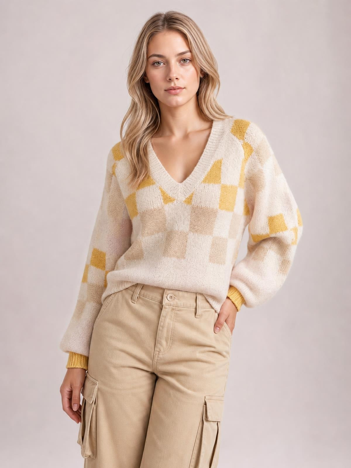 A model poses in a cream and mustard checkered V-neck sweater with voluminous lantern sleeves, ribbed cuffs, and a relaxed silhouette.