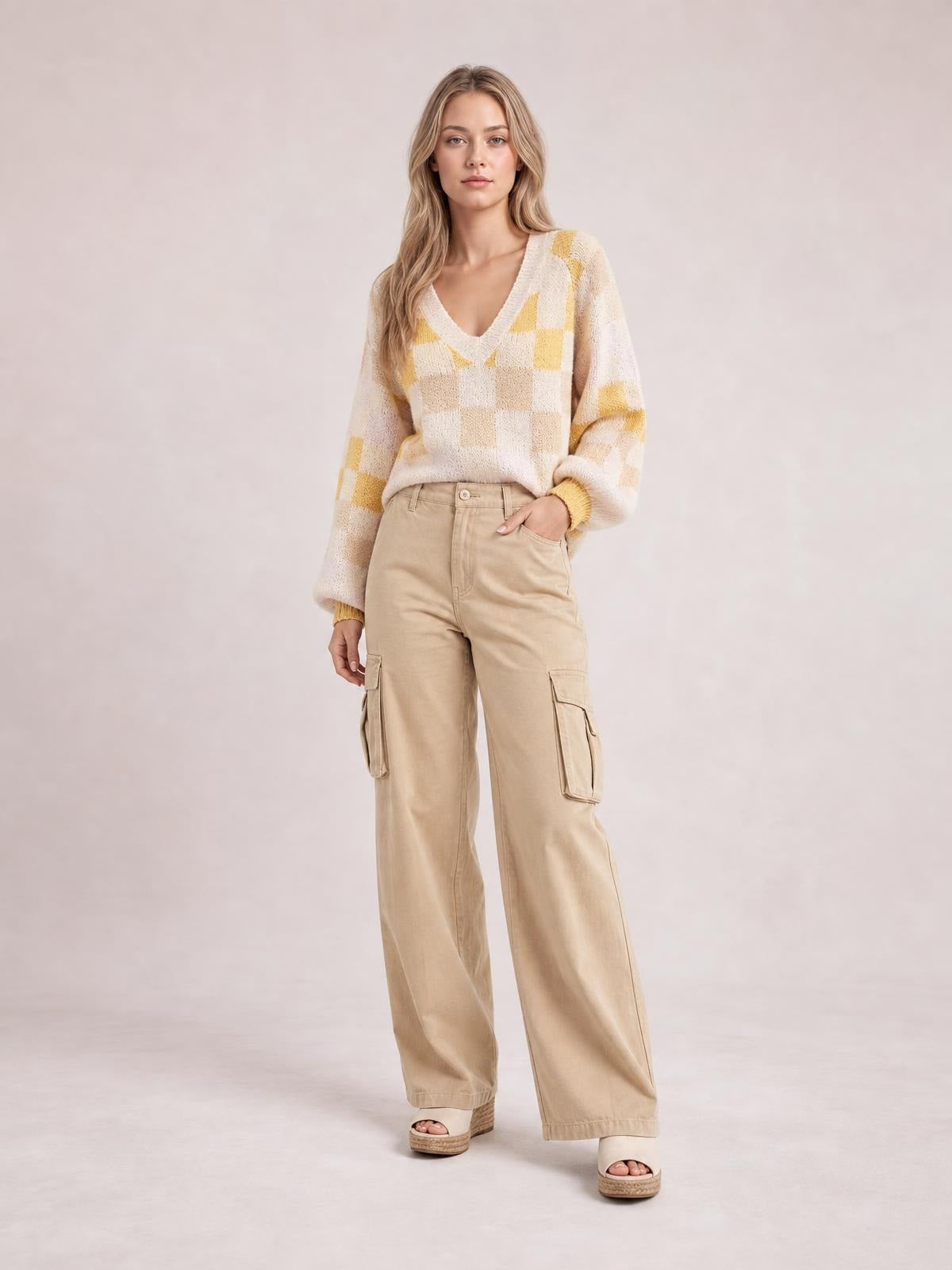 Model stands with one hand in her pocket wearing a cream and yellow checkered V-neck sweater with relaxed lantern sleeves and ribbed trim.