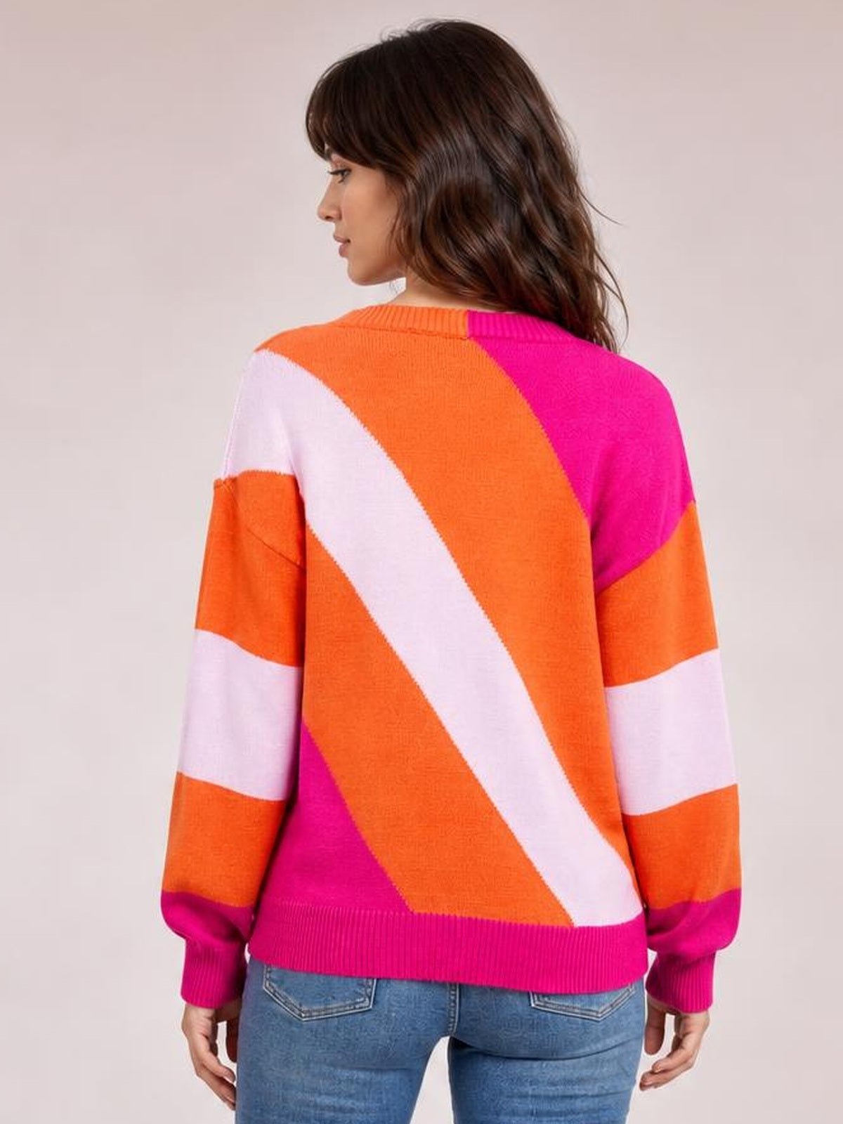 Model stands in a back view wearing a colorful ribbed round neck sweater with orange, pink, and white color-block panels, long sleeves, and a regular silhouette.