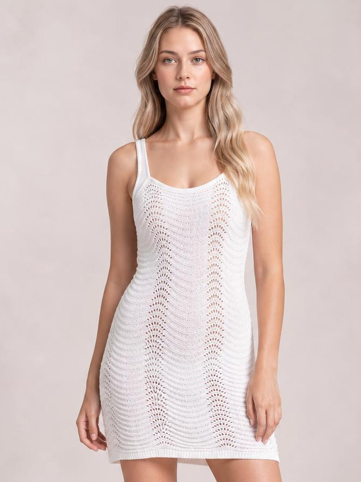 Model standing in a white sleeveless cover-up dress with a fitted mini silhouette, straight neckline, and sheer openwork knit construction.