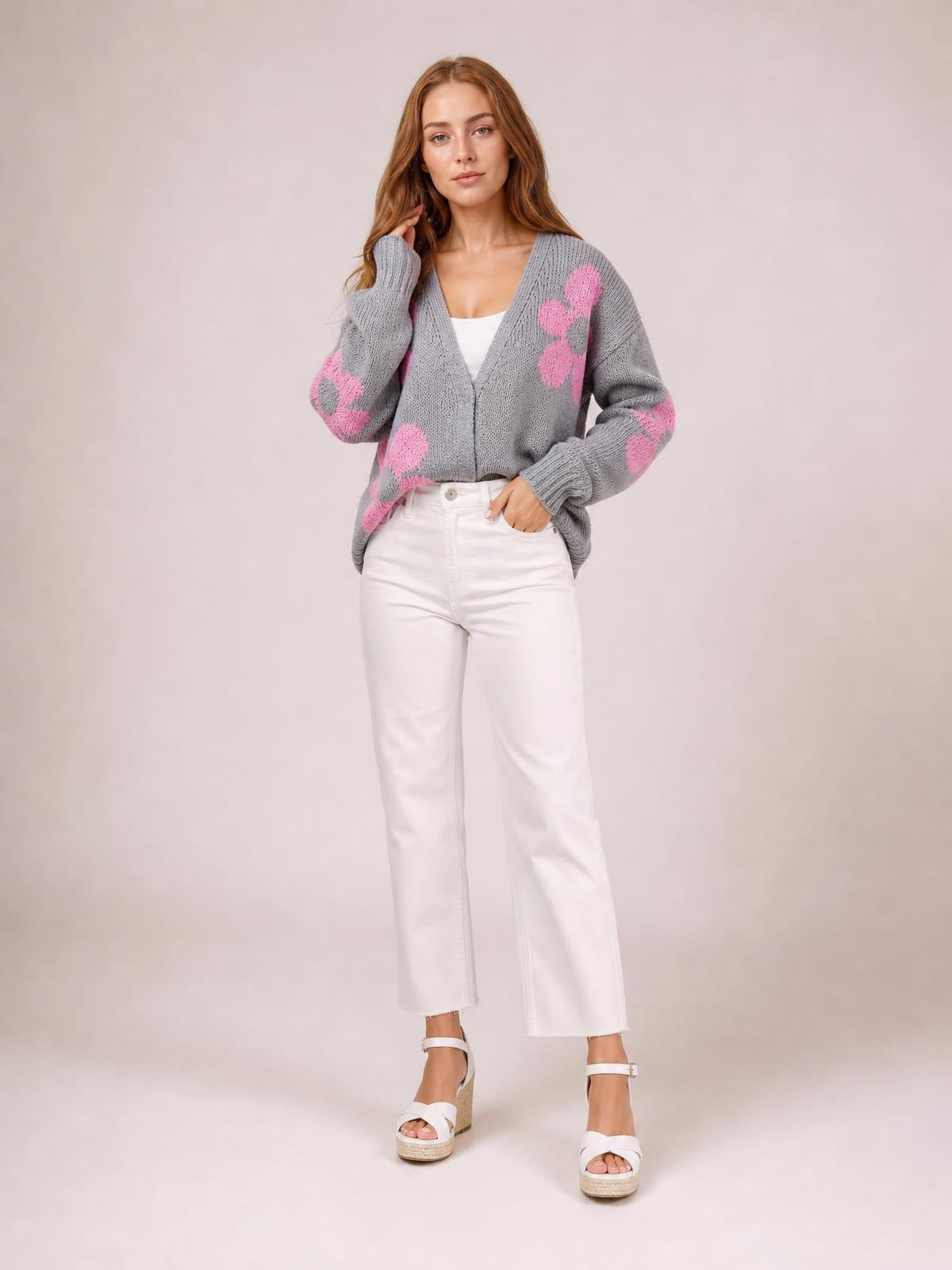Model poses in a gray open-front long-sleeve cardigan with pink flower motifs, a V-neckline, ribbed cuffs, and a relaxed silhouette.