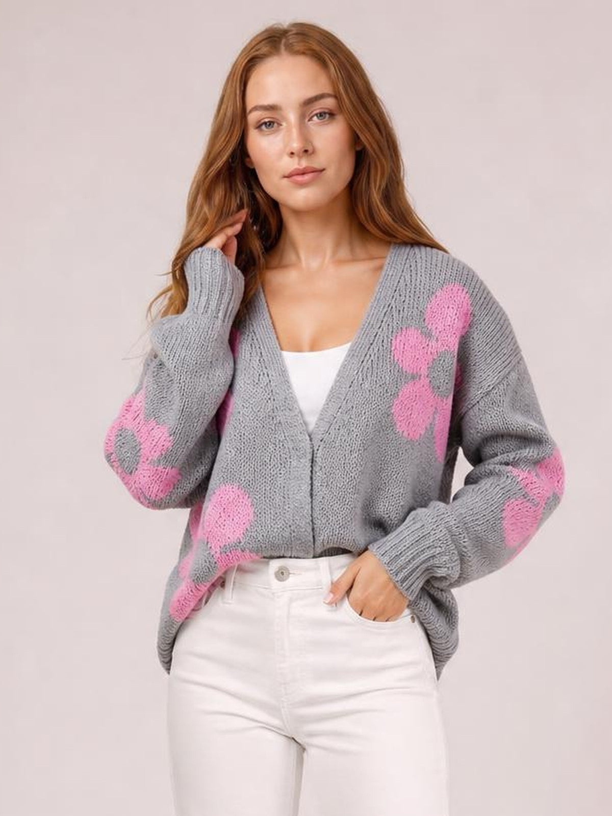 A model poses in a relaxed gray open-front long-sleeve cardigan with pink flower motifs, chunky knit texture, ribbed cuffs, and a softly oversized silhouette.