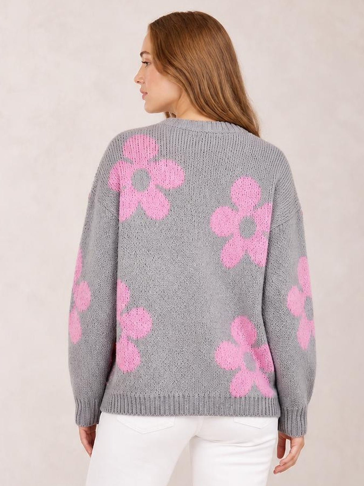 Model shown from the back wears a gray knit flower cardigan with pink floral motifs, long sleeves, a relaxed silhouette, and ribbed cuffs and hem.